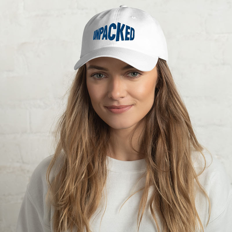 female model wearing a white dad hat with the Unpacked brand logo sewn in blue thread  Edit alt text