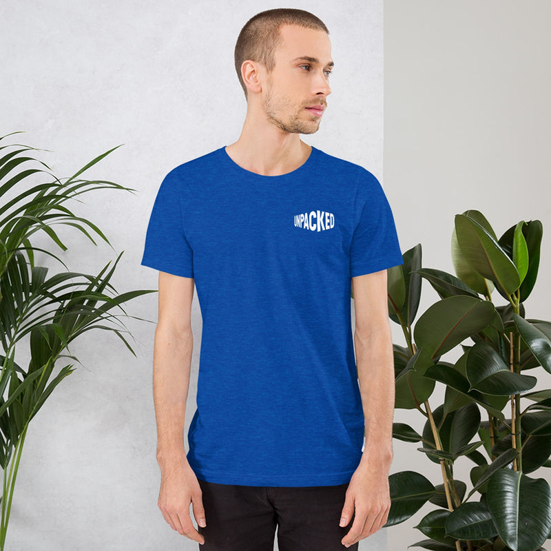 male model standing between two ferns wearing a blue t-shirt with the Unpacked brand logo in white printed small onto the pocket area