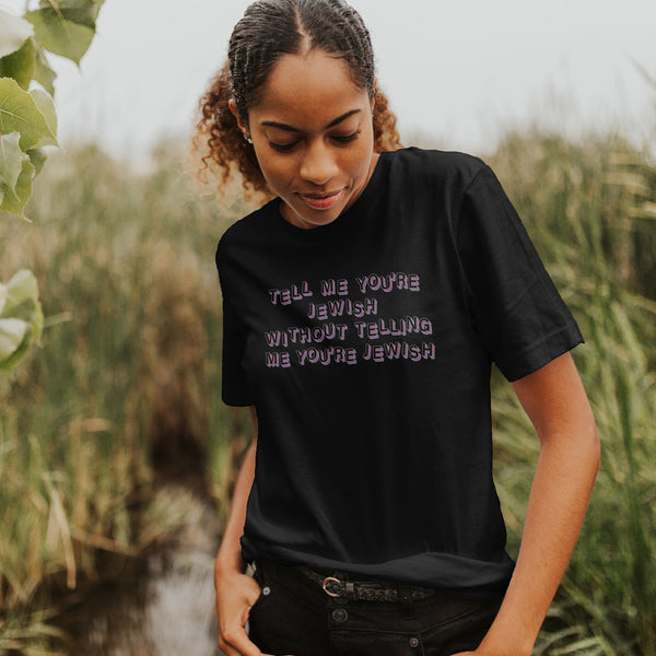 female model in field, wearing a black shirt that reads "tell me you're jewish without telling me you're jewish"